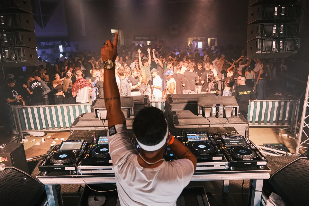 DJ hinter den Decks, davor tanzt die Crowd in warmem Dunst